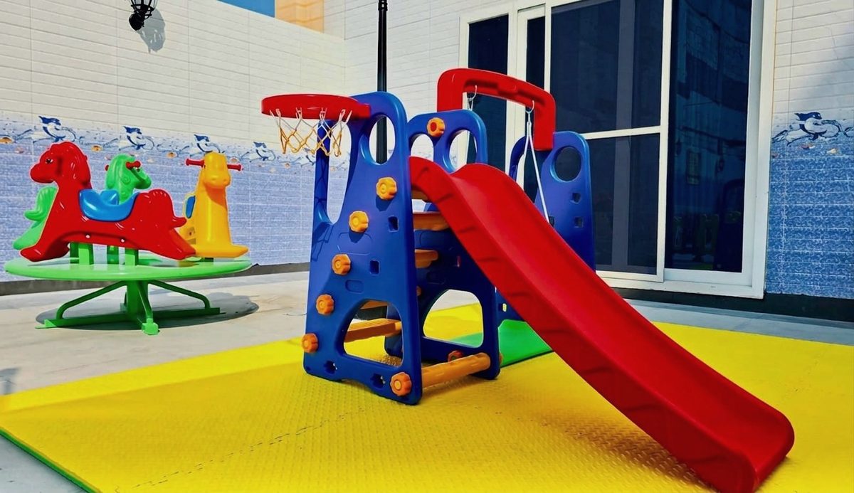 Children's play area with a slide, a basketball hoop and ride-on animals on a padded yellow floor