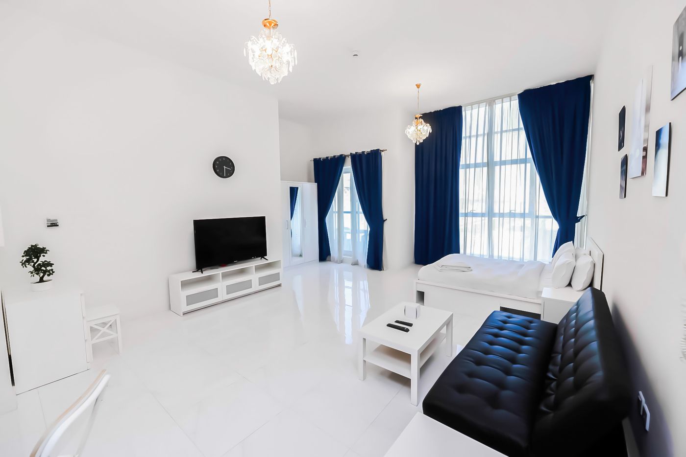 Studio with a king bed, a sofa bed, a wardrobe and tall windows with navy curtains